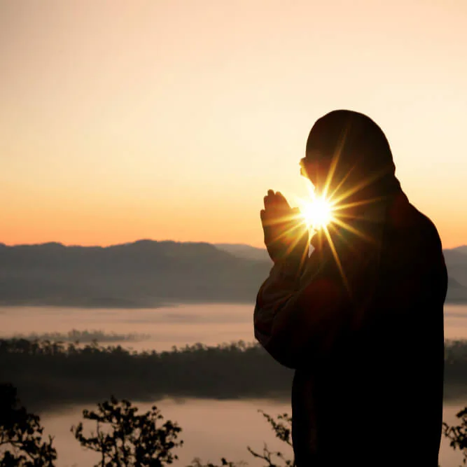 A woman in silhouette with her hands together at sunrise