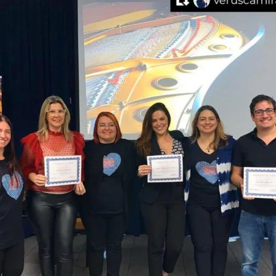 Six course participants holding their certificates in front of the projection screen