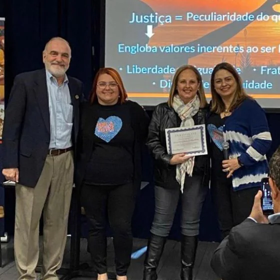 A certificate handed over on stage, with a slide on justice and human values behind