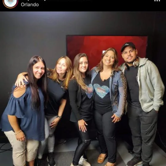 Five people together in a recording studio in front of a monitor