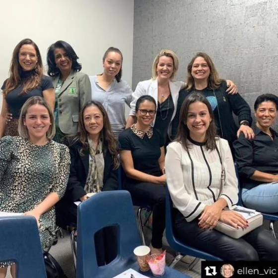 Eleven women gathered in a meeting room, some seated and some standing